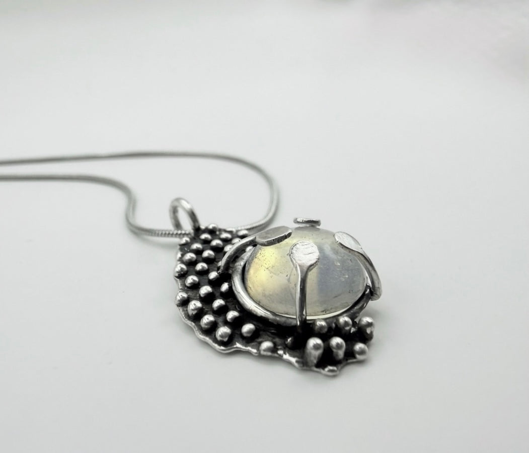 Close-up angle shot of a Dewdrop Moonstone Necklace in sterling silver with a luminous domed moonstone and droplet-textured setting on a silver snake chain