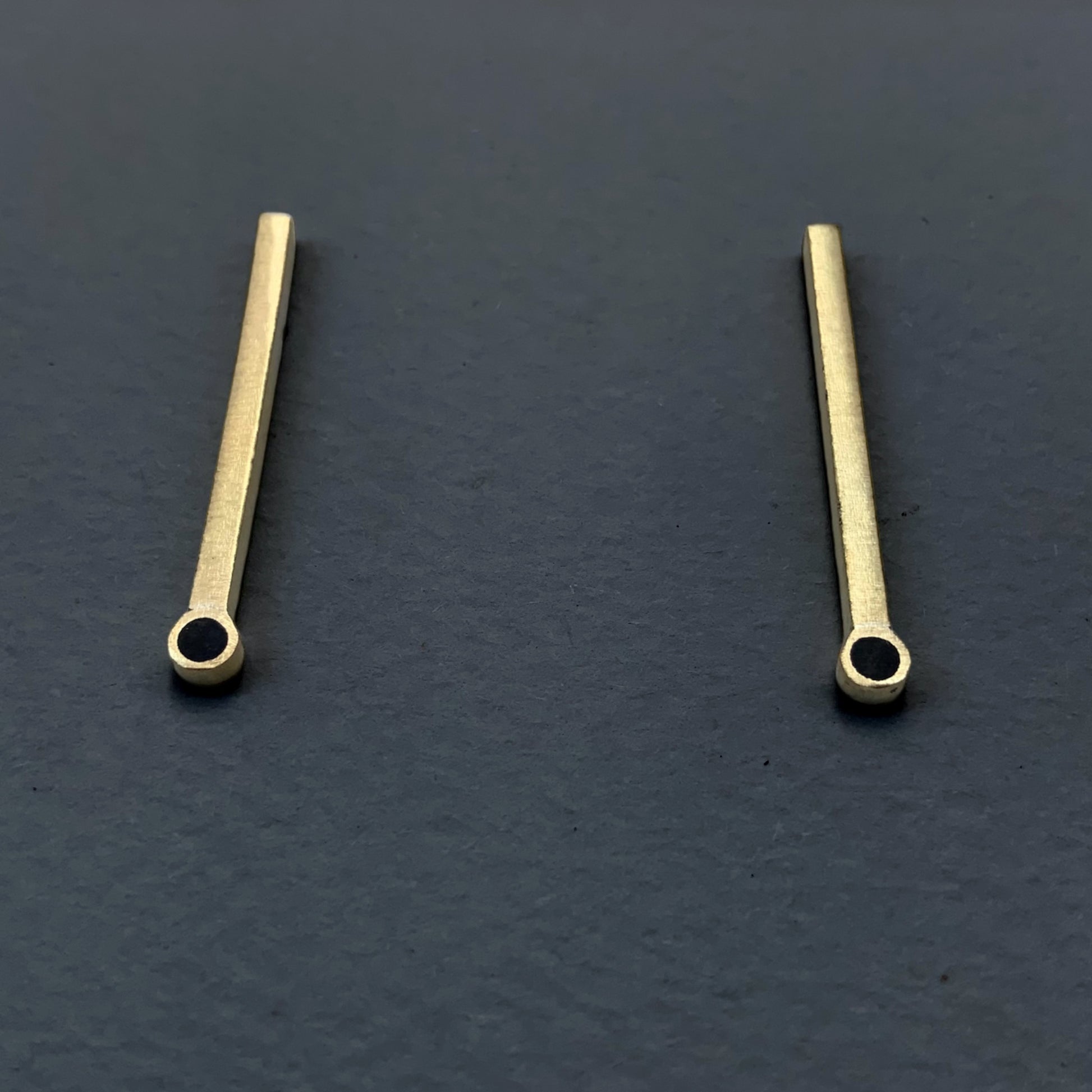 Handcrafted brass bar earrings featuring a circular cutout at the bottom, styled on a dark gray background for a bold contrast