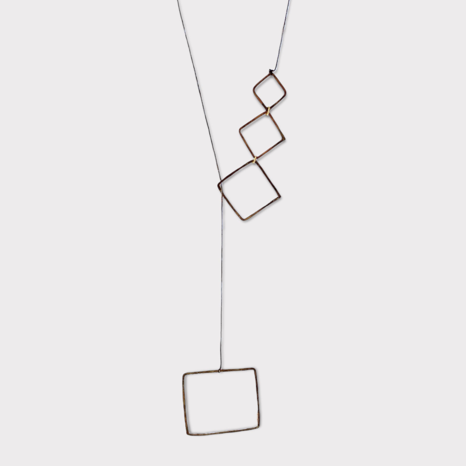 A handcrafted necklace featuring cascading open brass squares linked together, suspended on a minimalist cord, displayed on a clean white background to highlight its geometric design