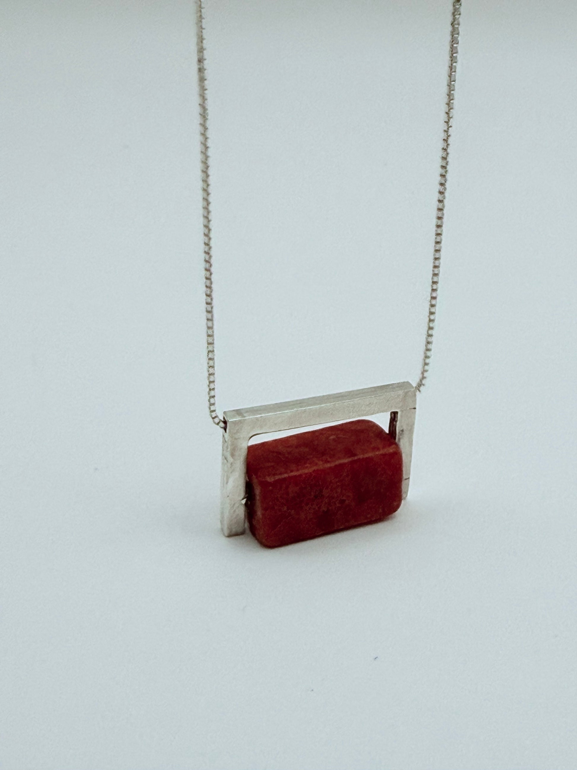 Geometric sterling silver and coral necklace with a structured silver frame hugging a red coral block, with a box silver chain on a white background