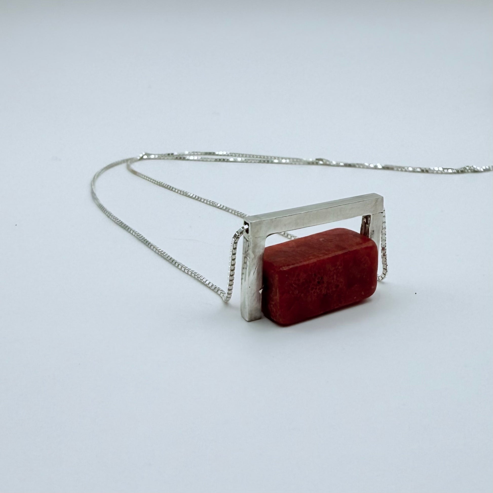 Close-up of the Geometric Sterling Silver & Coral Necklace with a structured silver frame hugging a red coral block on a white background