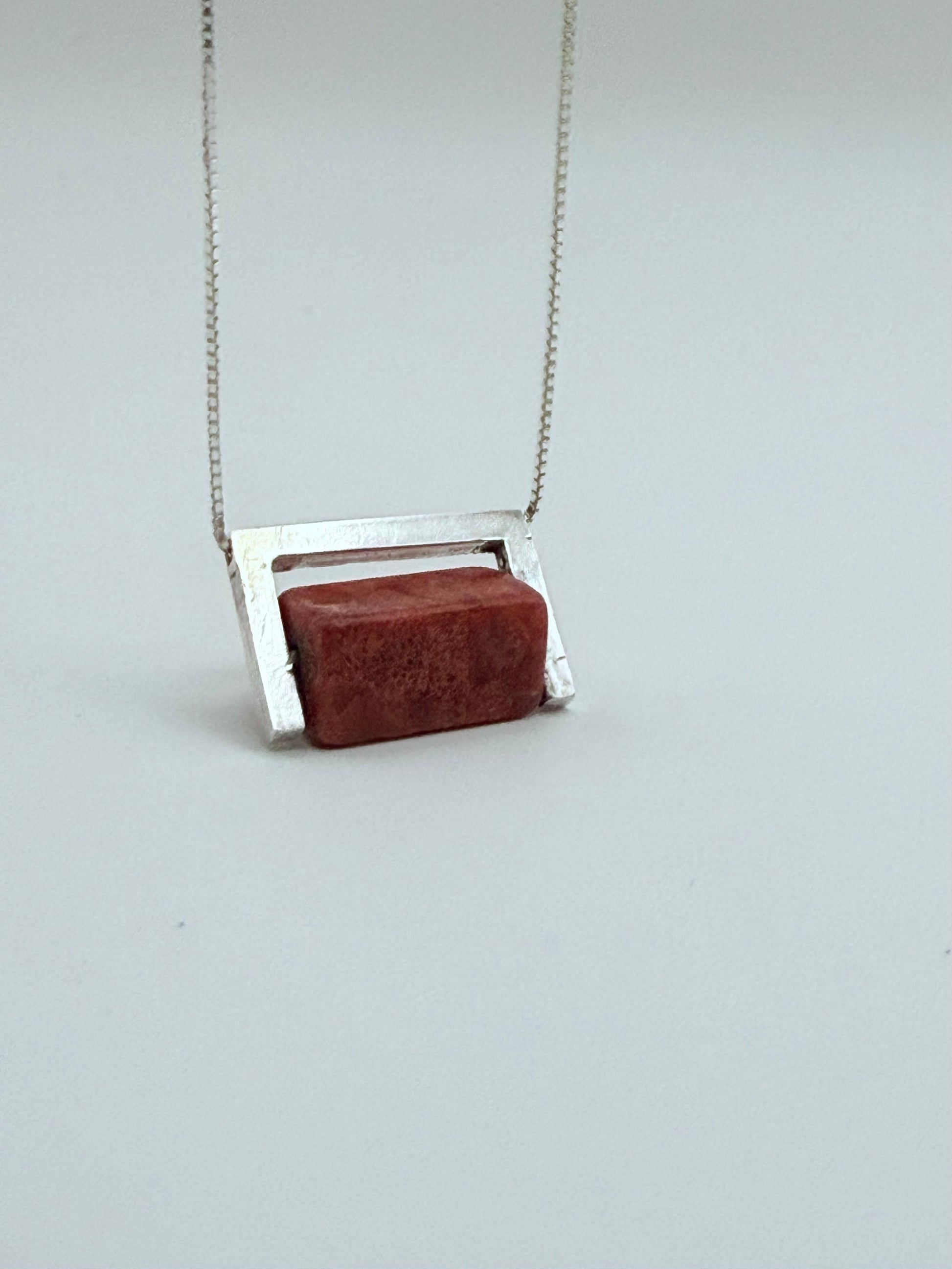 Close-up front view of the Geometric Sterling Silver & Coral Necklace with a red coral block set in a structured sterling silver frame on a white background