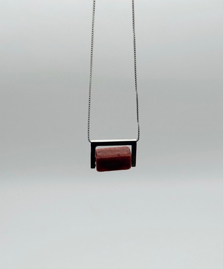 Hanging front view of the Geometric Sterling Silver & Coral Necklace with a red coral block set in a structured sterling silver frame on a white background