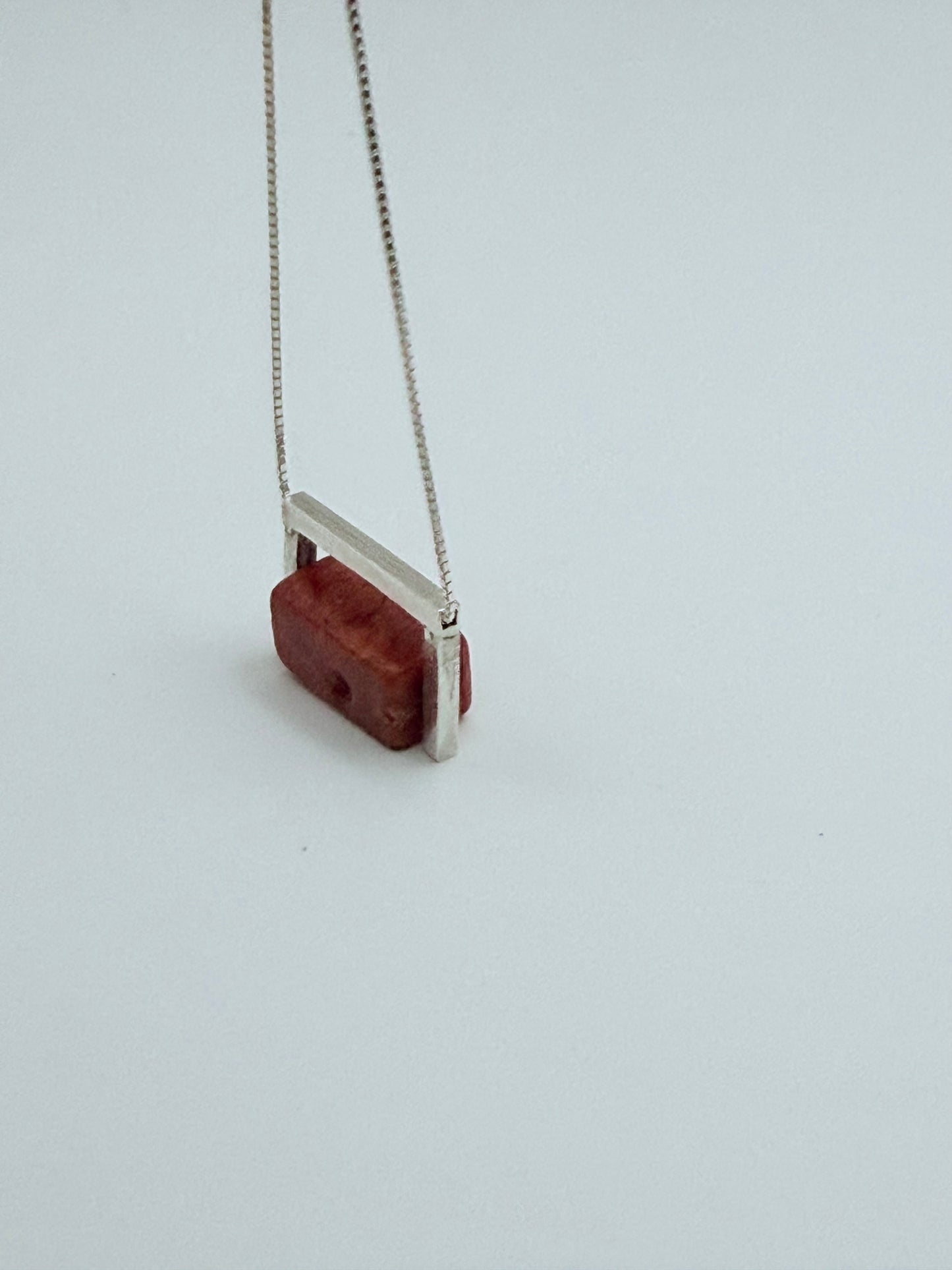 Side angle view of the Geometric Sterling Silver & Coral Necklace showing the structured sterling silver frame around the red coral block on a white background