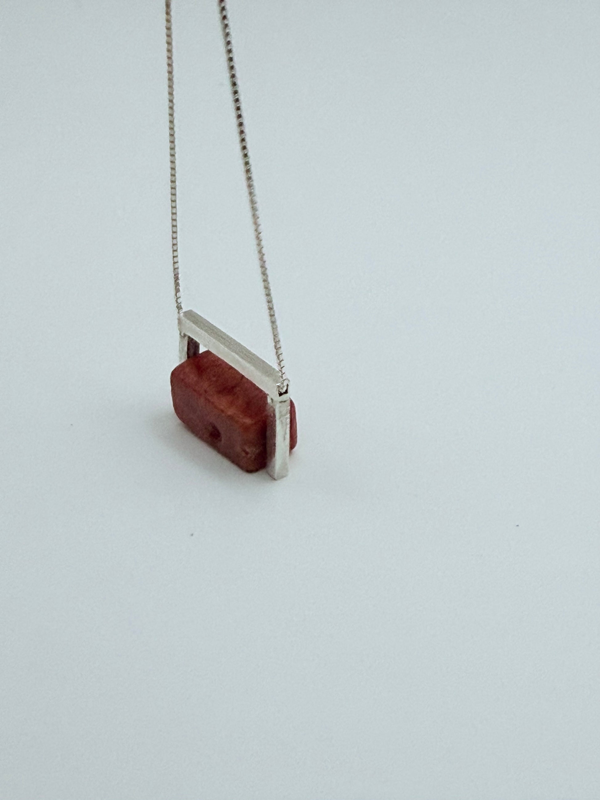Side angle view of the Geometric Sterling Silver & Coral Necklace showing the structured sterling silver frame around the red coral block on a white background