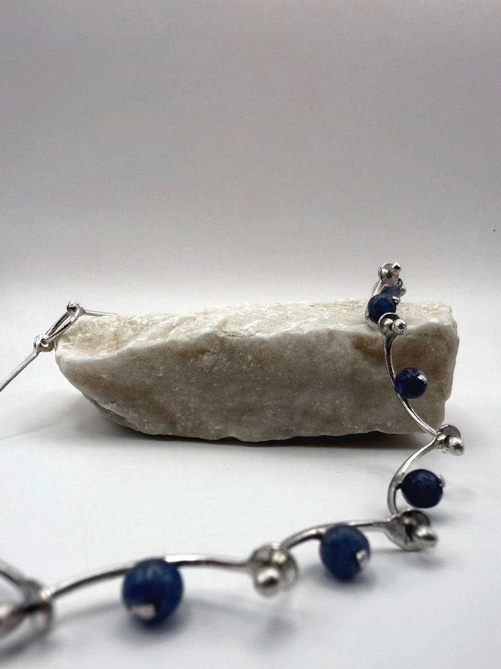 Close-up of a handmade sterling silver necklace with hammered details and blue aventurine beads, inspired by sea waves, styled on a natural stone.

