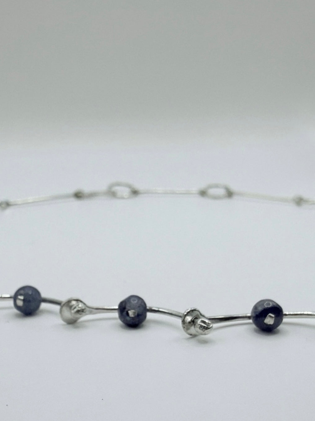 Close-up of a handmade sterling silver necklace with blue aventurine beads and hammered, wave-inspired links, minimalist Greek jewelry.
