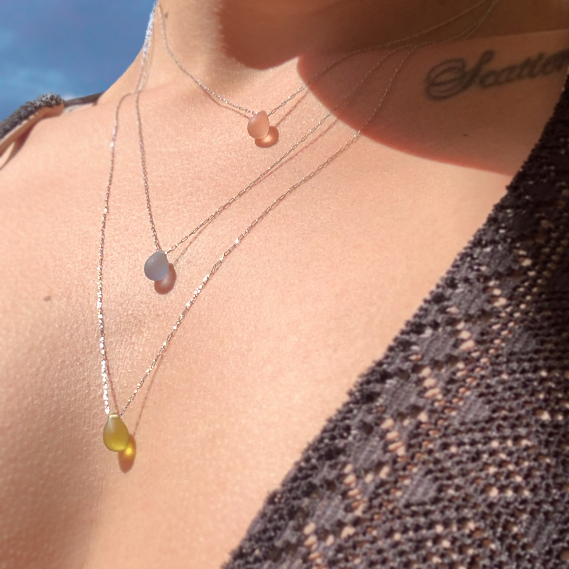 decolletage-of-woman-wearing-three-different-lengths-minimalist-necklace-pendants-with-dropshaped-frosted-glass-and-silver-stainless-steel-chain-product-photography-jewelry-by-meow-iris-necklaces-iris-collection