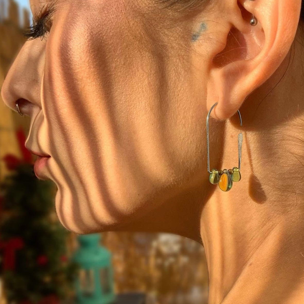 woman-profile-closeup-wearing-pair-of-silver-hoop-earrings-tulipd-shaped-with-three-multicolored-glass-teardrop-beads-hanging-from the-bottom-jewelry-by-meow-iris-collection-aurora-earrings