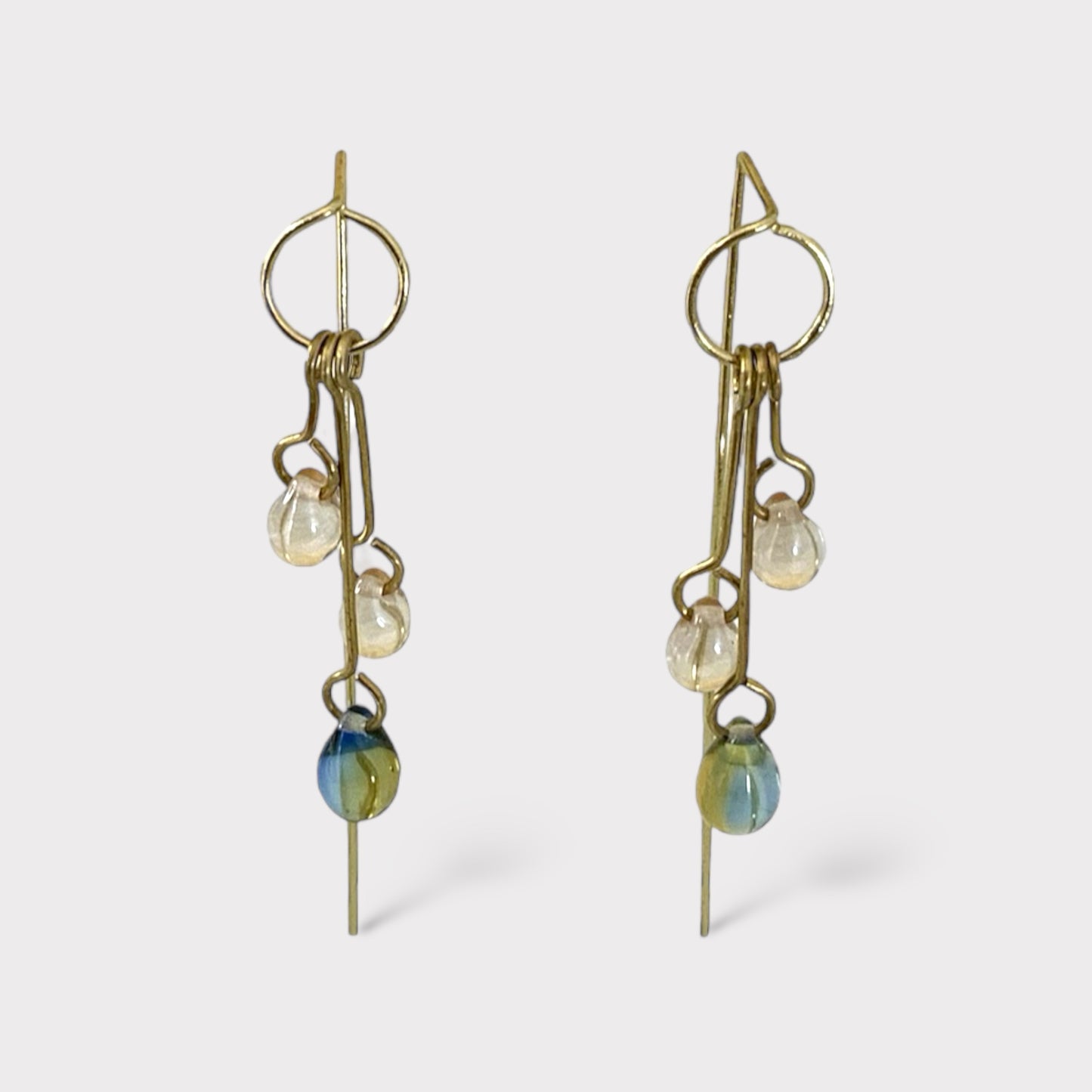 A pair of handcrafted long dangle earrings featuring clear and gradient glass pendants in shades of green and blue, suspended on brass hooks, displayed on a white background for a minimalist presentation.