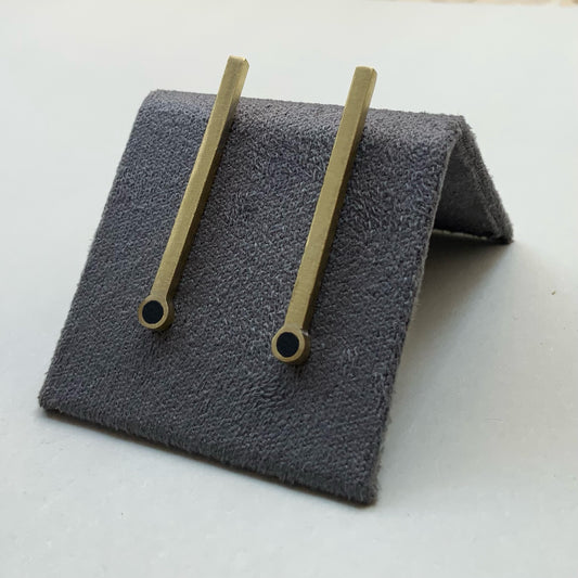 A pair of minimalist brass bar earrings with a circular cutout at the base, elegantly presented on a soft gray stand to highlight their sleek design