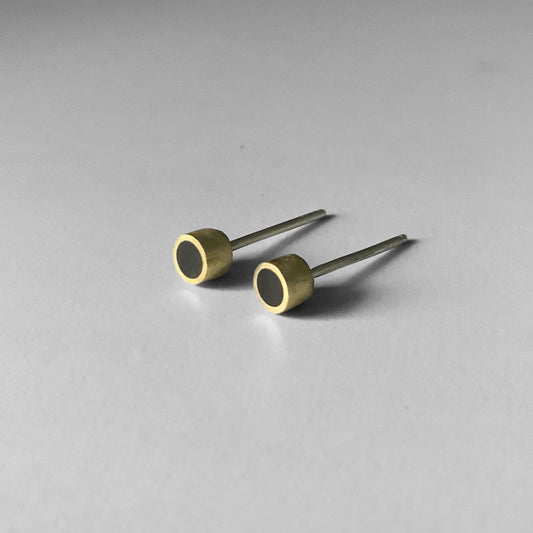 A pair of handcrafted brass stud earrings with a black circular inlay, displayed on a light gray surface to emphasize their sleek and minimalist design