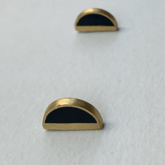  A pair of handcrafted brass half-circle earrings with black accents, displayed on a light gray background to highlight their minimalist and geometric design