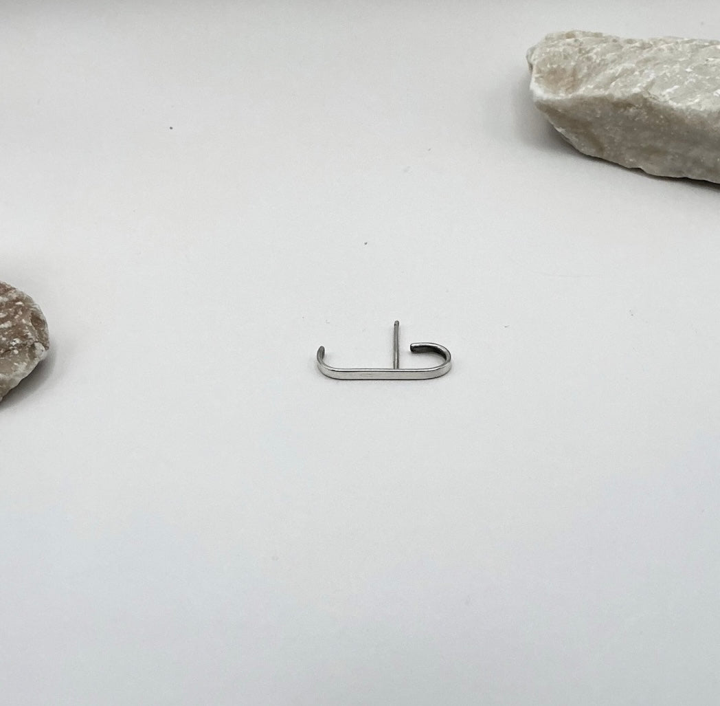 Minimalist Curve Sterling Silver Ear Hook shown in a flat lay with light stone props on a white background