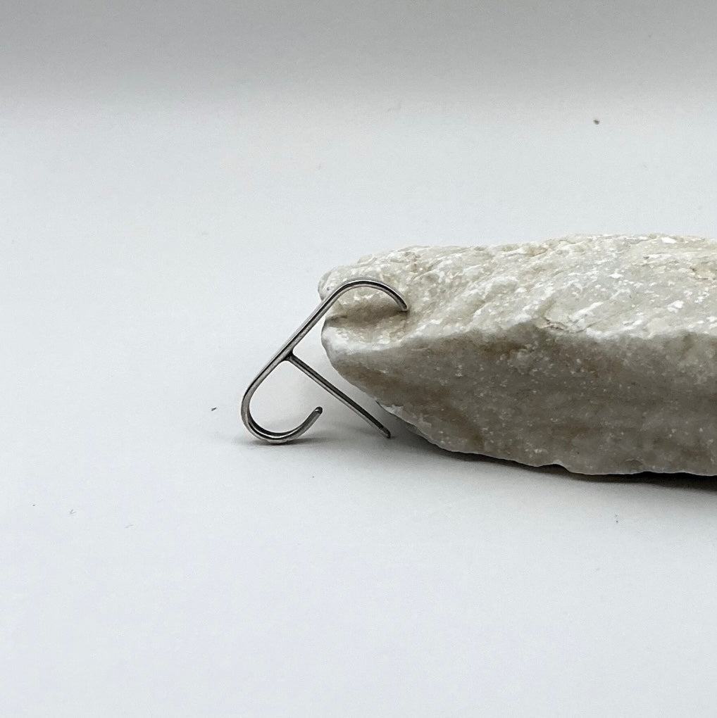 Minimalist Curve Sterling Silver Ear Hook with a sleek curved open design leaning on a marble on a light gray background