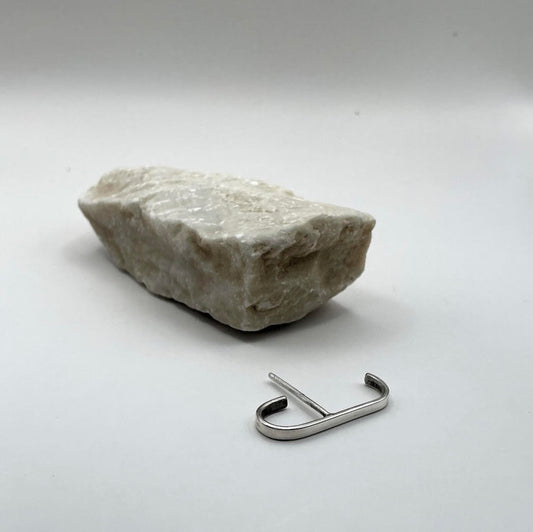 Minimalist Curve Sterling Silver Ear Hook in a styled flat lay with a light stone on a white background