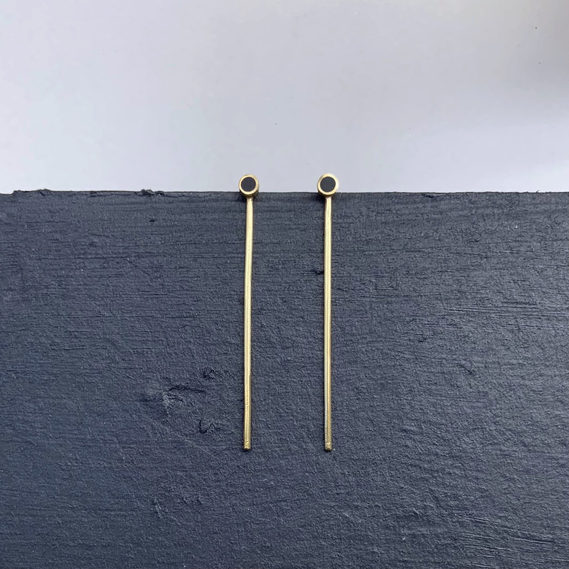 Handmade gold earrings featuring a long minimalist bar with black circular accents, designed for contemporary styles