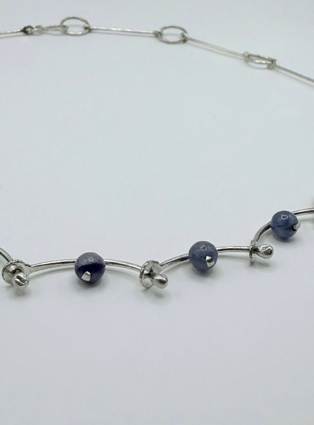 Close-up of a handmade sterling silver necklace with blue aventurine beads and hammered, wave-like links, minimalist Greek jewelry design.
