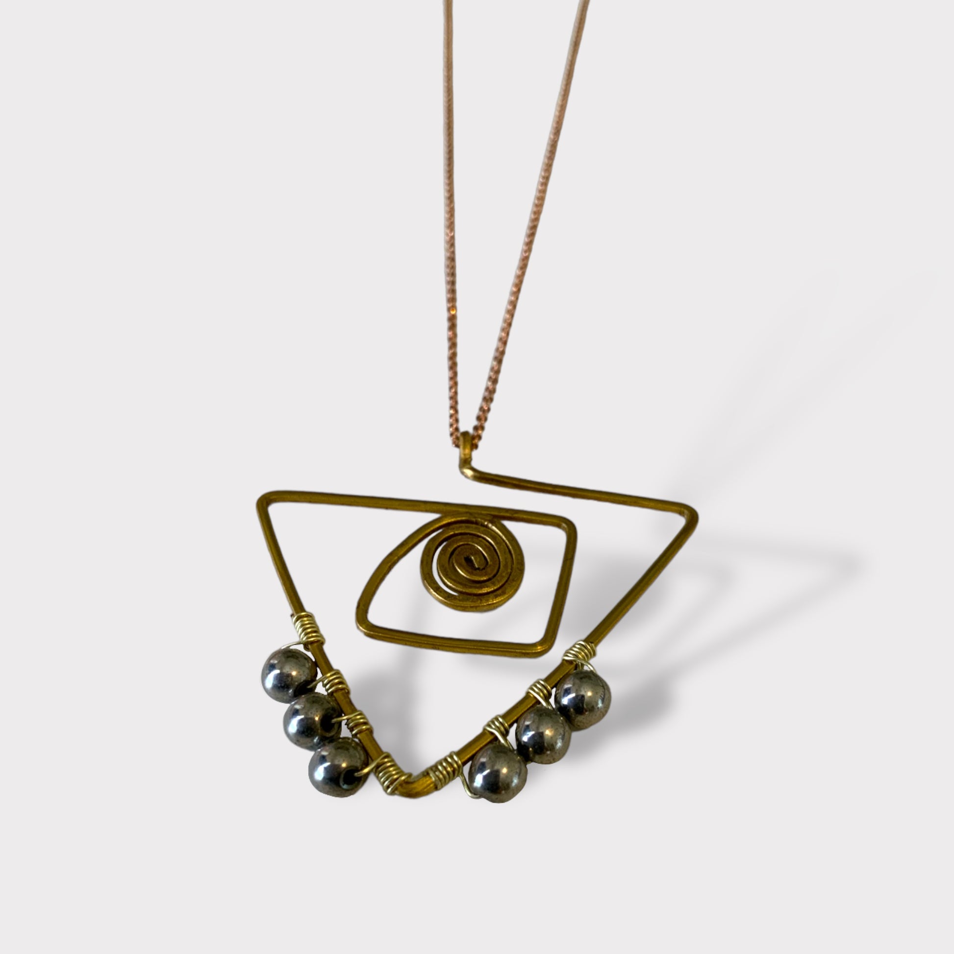 A minimalist brass necklace with an abstract triangle frame, spiral detail, and metallic bead accents, styled on a white background to highlight its unique and artistic design