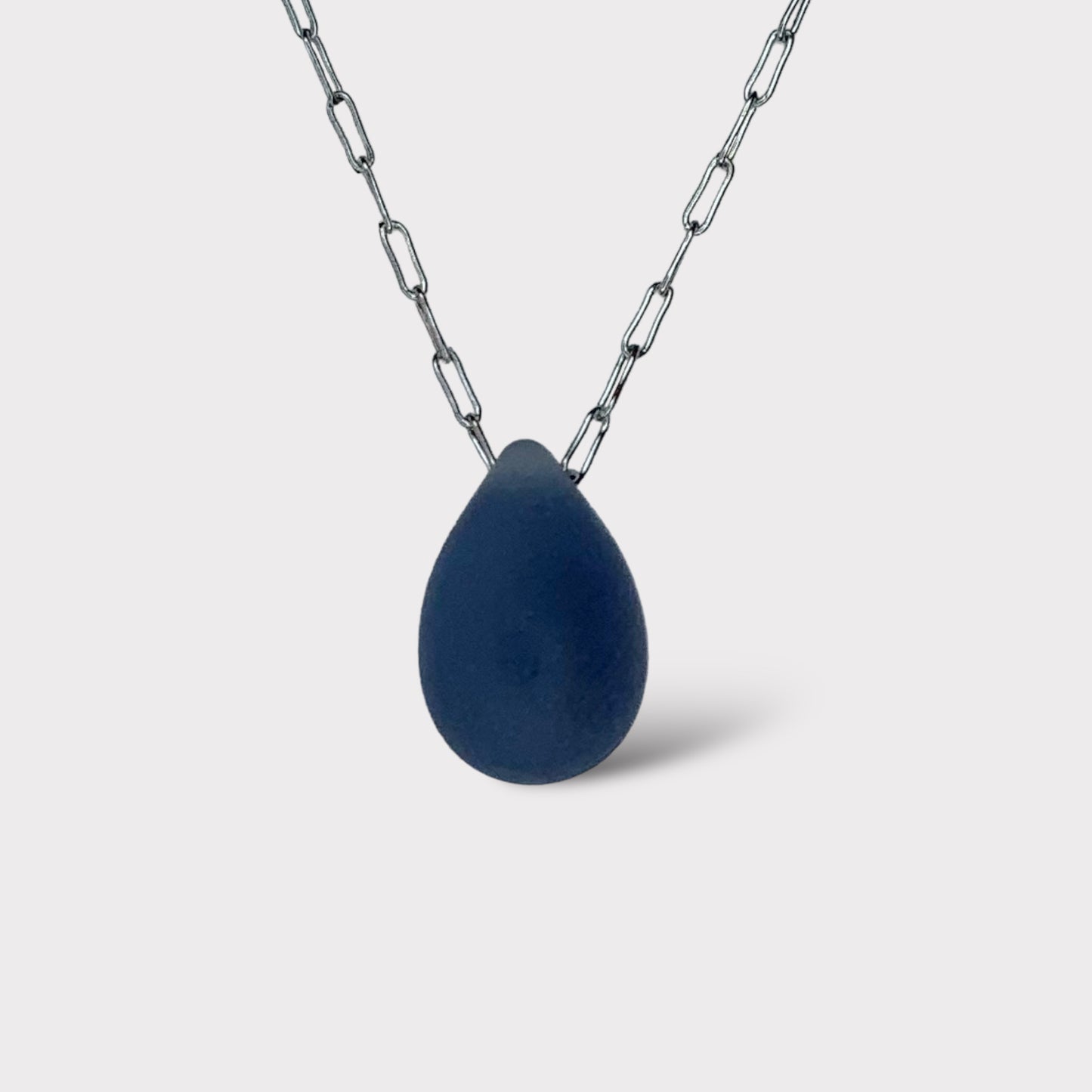 A soft matte Montana blue teardrop-shaped glass pendant, suspended on a stainless steel chain, displayed on a white background for a minimalist design.