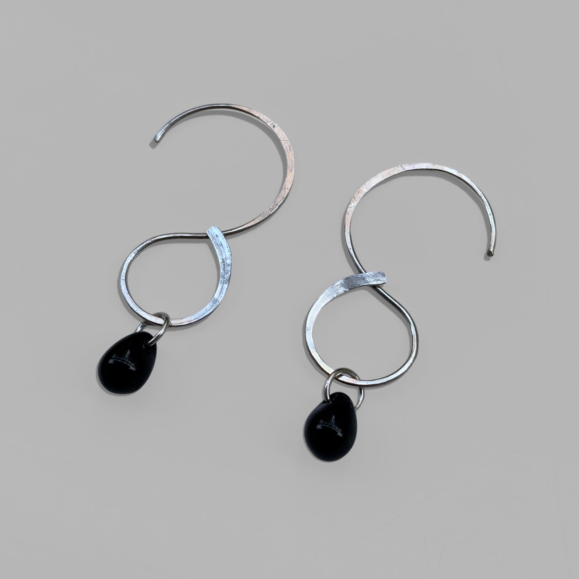  small-minimalist-hoop-sterling-silver-earrings-with-black-glass-teardrop-beads-product-photography-jewelry-by-meow-eclipse-collection-haumea-earrings-grey-background