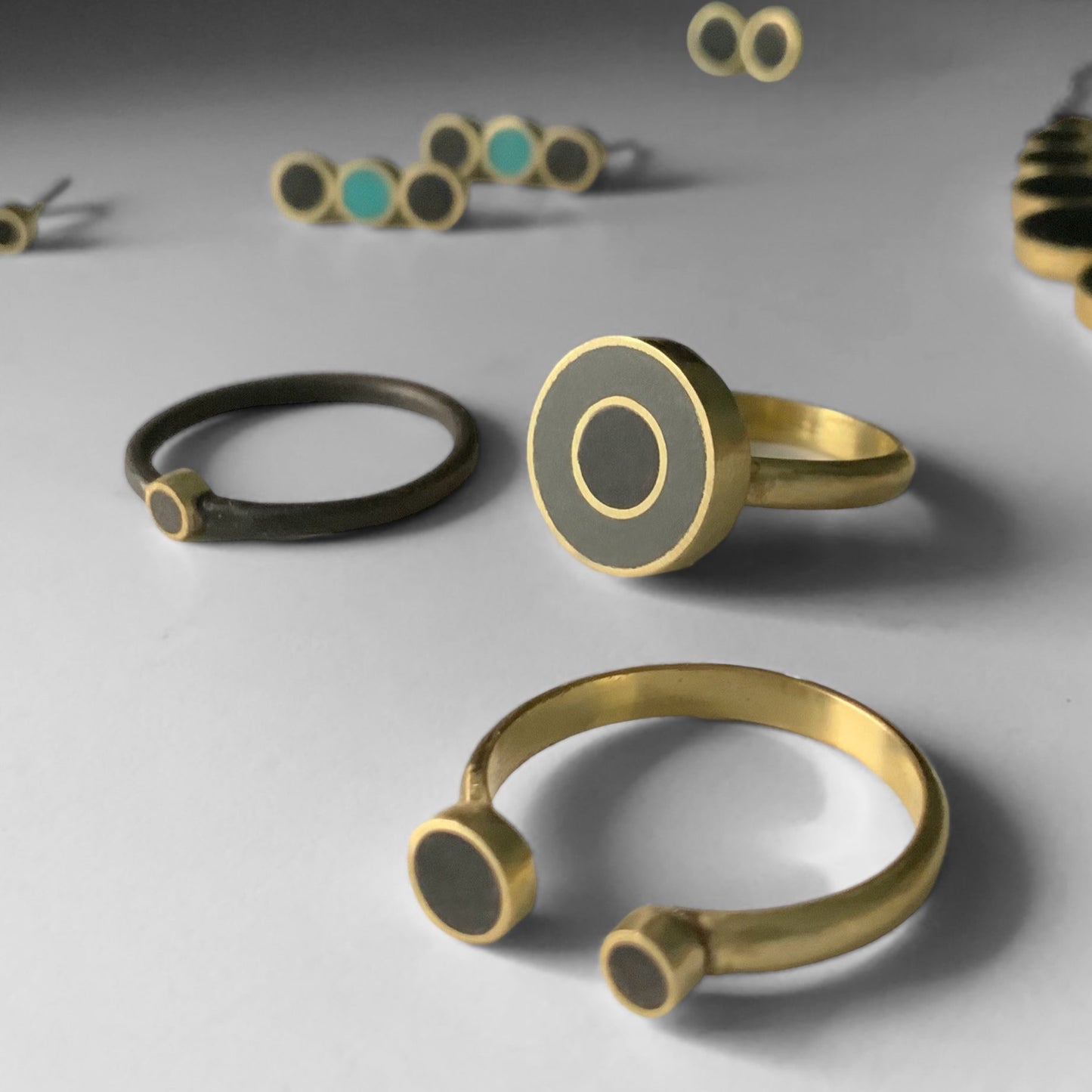 close-up-collection-handmade-artisan-greek-golden-minimalist-rings-and-earrings-with-circle-shapes-with-dark-grey-turqoise-and-black-polymer-clay-inlay-on-a-grey-surface-jewelry-by-meow-dusk-and-dawn-collection 