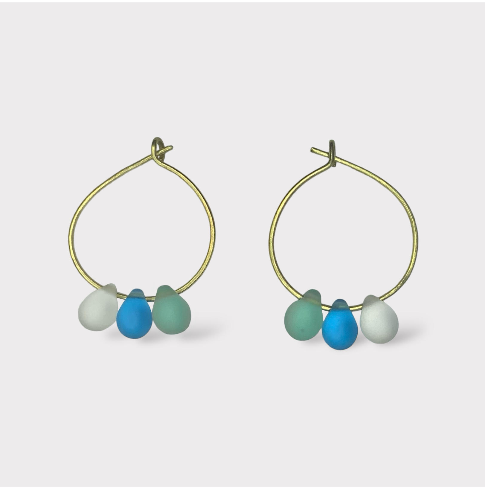 Playful gold hoop earrings adorned with aqua, turquoise, and seafoam green seaglass charms. A breezy and refreshing design reminiscent of seaside popsicles.

