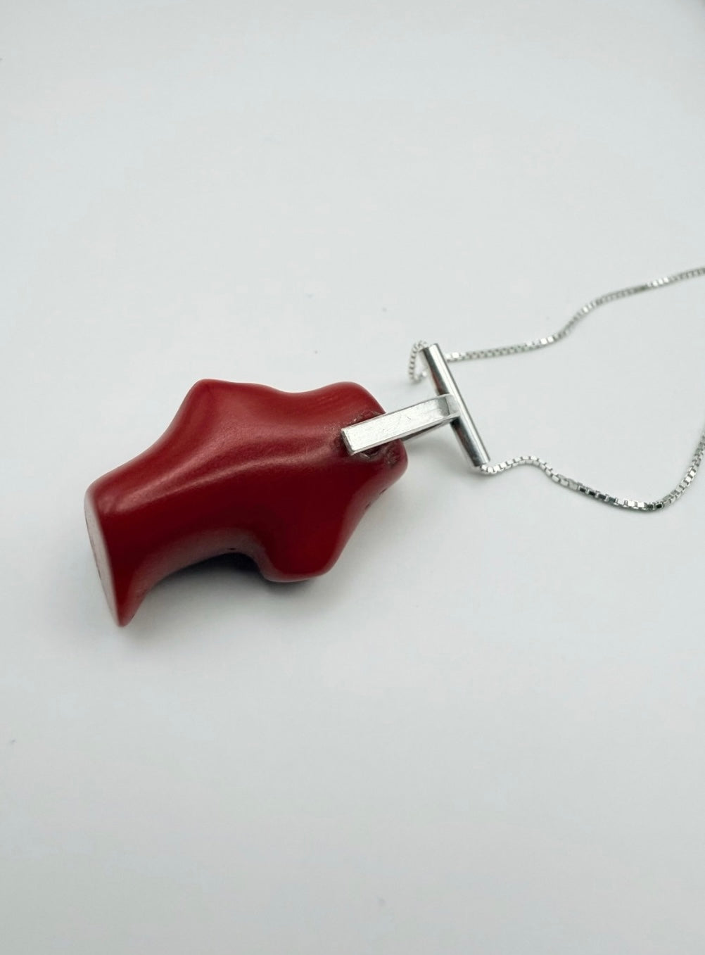 Top view of the T-bar Coral Sterling Silver Necklace with a red coral pendant and sterling silver T-bar bail on a box chain with a light gray background