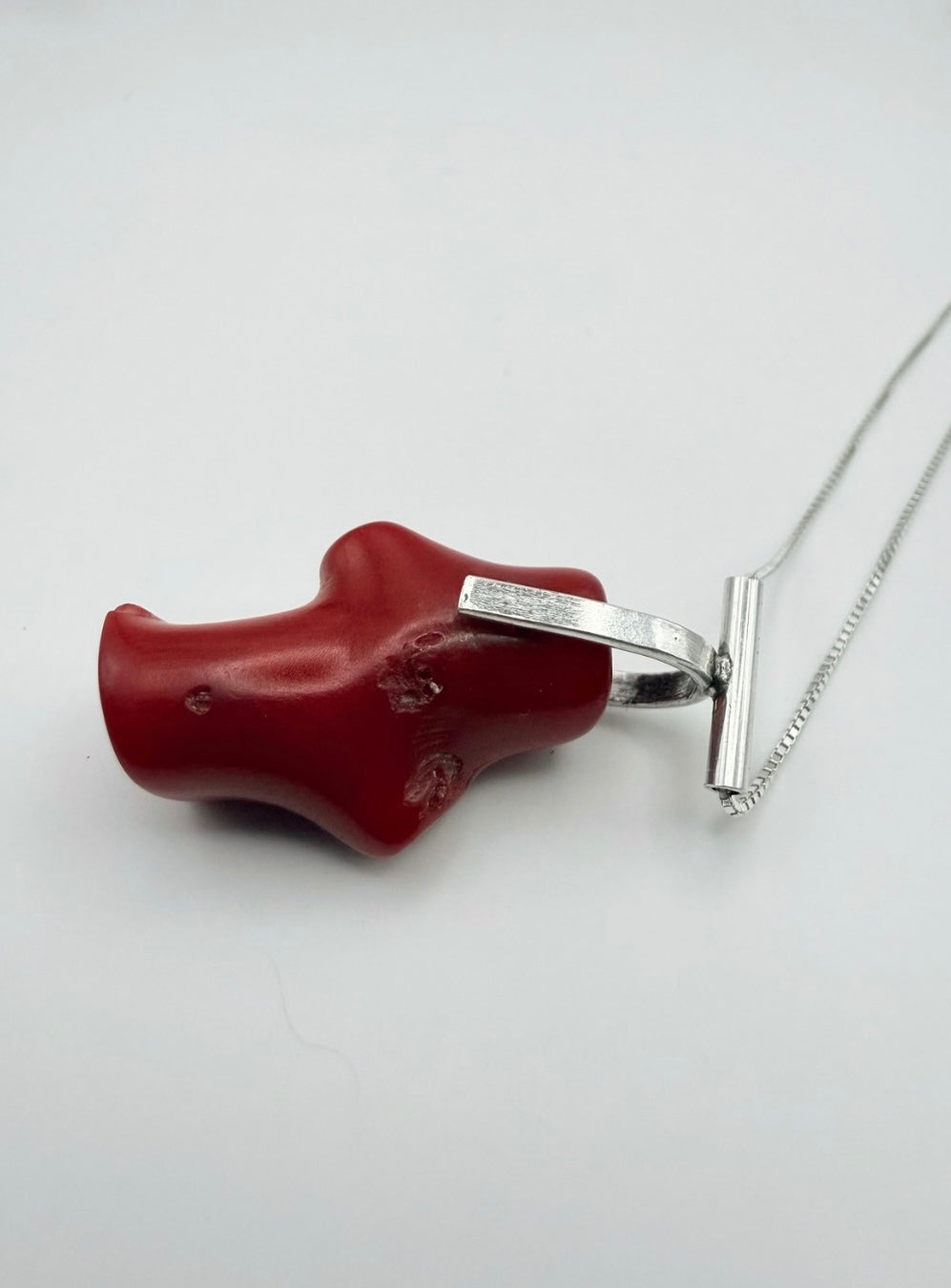 Side view of the T-bar Coral Sterling Silver Necklace with a red coral pendant and sterling silver T-bar bail on a box chain with a light gray background