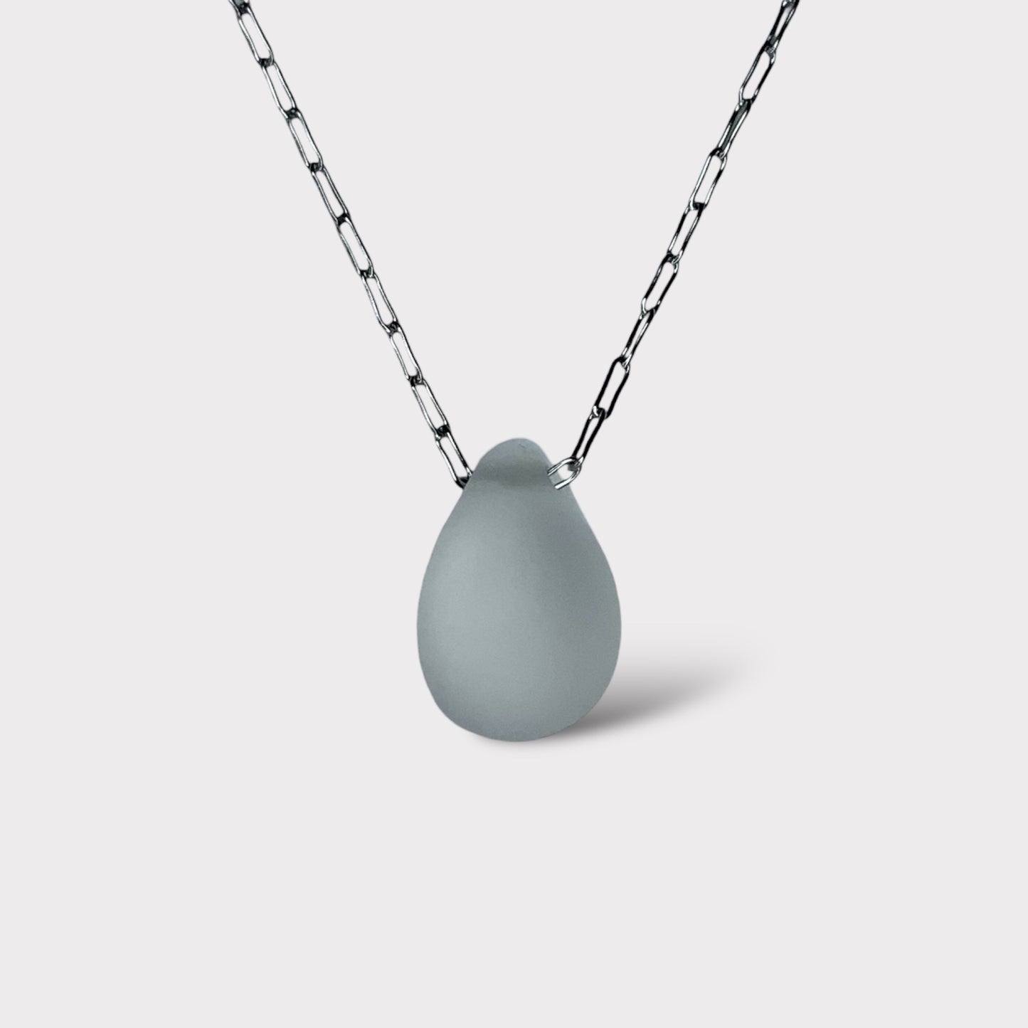 A frosted white matte teardrop-shaped glass pendant, elegantly suspended on a stainless steel chain, styled on a clean white background for a minimalist look.