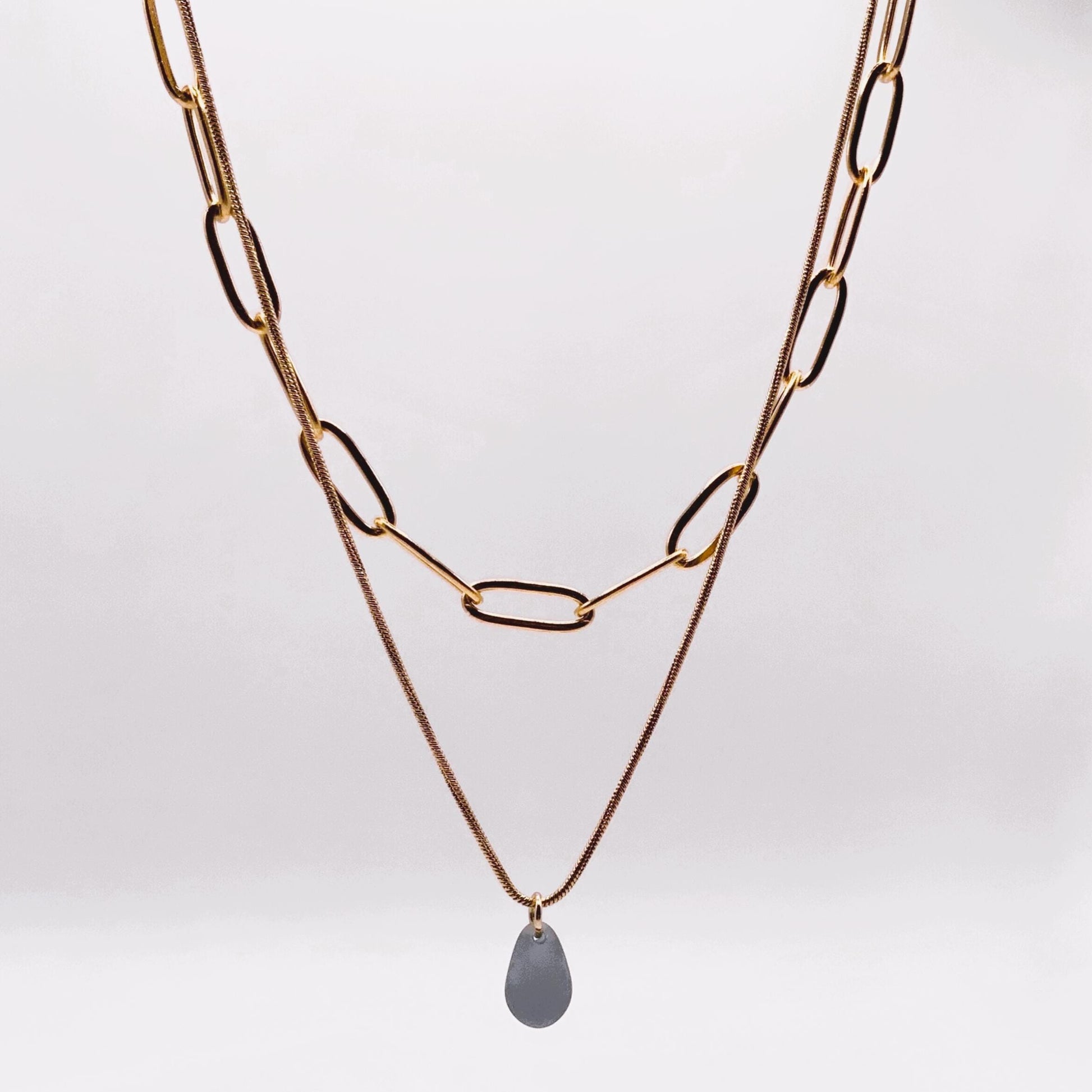 Close-up of a chunky gold cable chain and snake chain necklace with a frosted blue teardrop glass pendant. A bold yet minimalist piece, handcrafted in Greece, Jewelry by Meow.