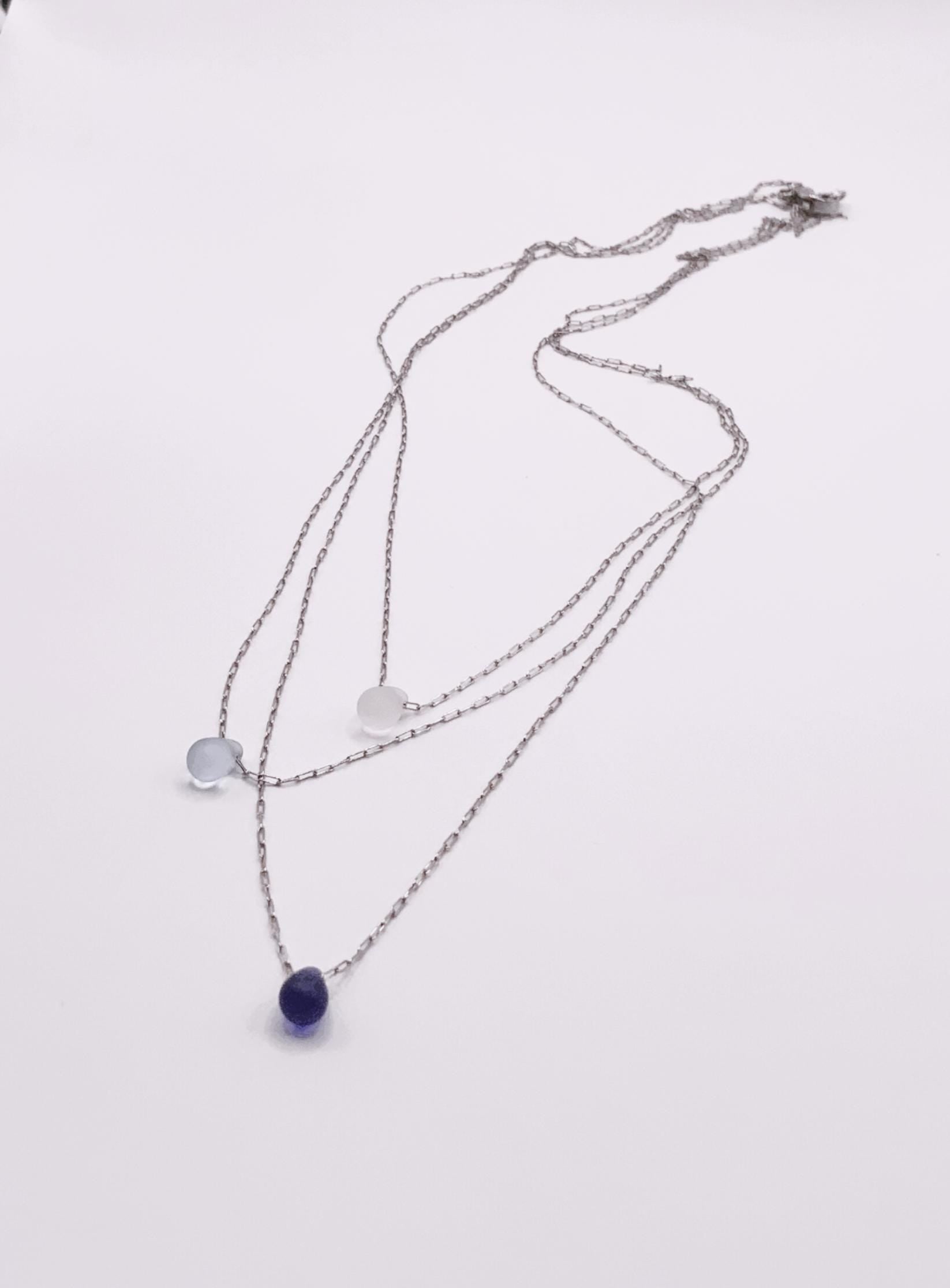 Flat-lay of three silver chain necklaces featuring frosted glass teardrop pendants in white, light blue, and deep blue on a clean white surface.