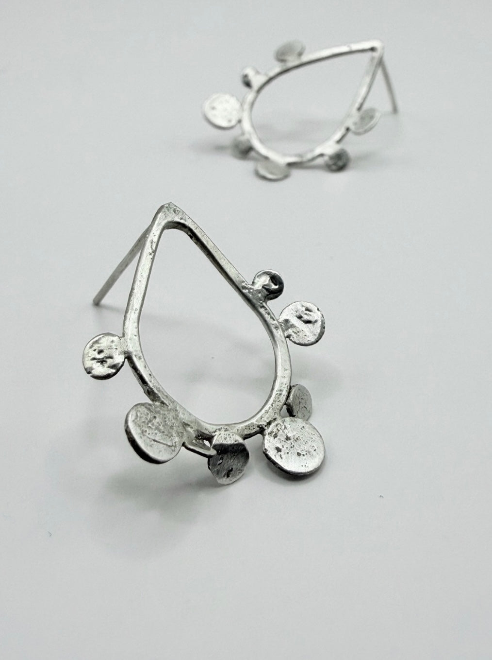 Close-up of sterling silver teardrop stud earrings with textured dot disc details on a white background