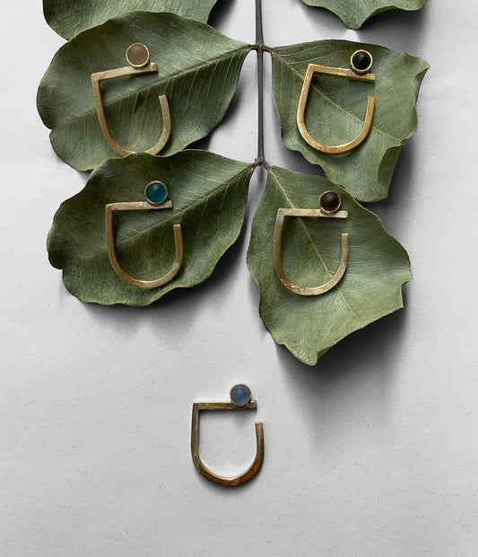 Handmade gold rings with colorful frosted glass cabochons, styled on green leaves for a natural and modern aesthetic against a white background.