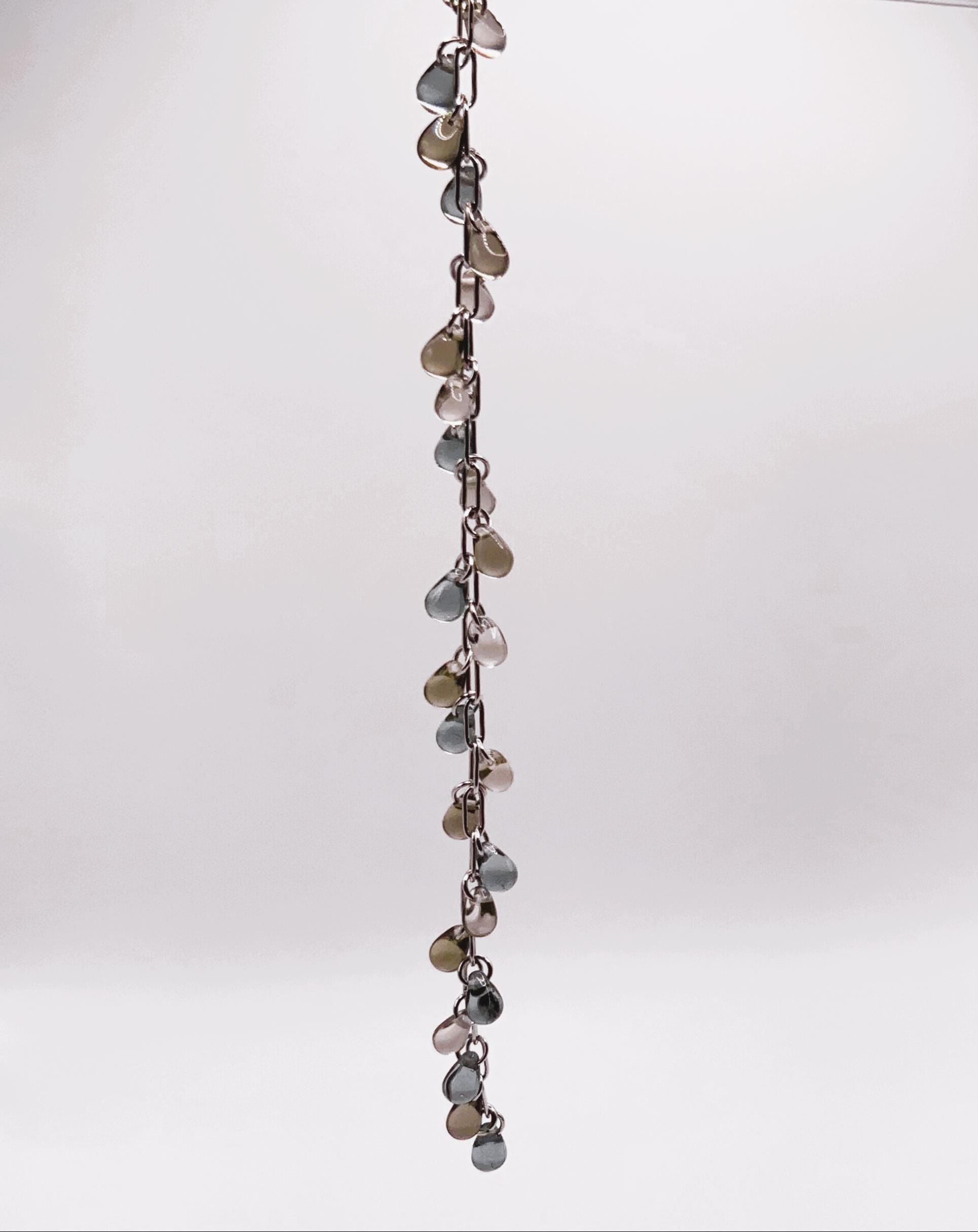 Silver chain bracelet with shiny glass teardrop charms in earthy tones, displayed vertically against a white background