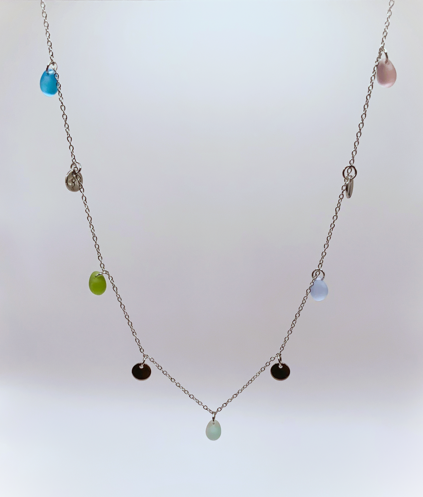 Minimalist silver necklace with frosted glass beads in pastel tones and small coin charms, handcrafted in Greece. A timeless design for all occasions.