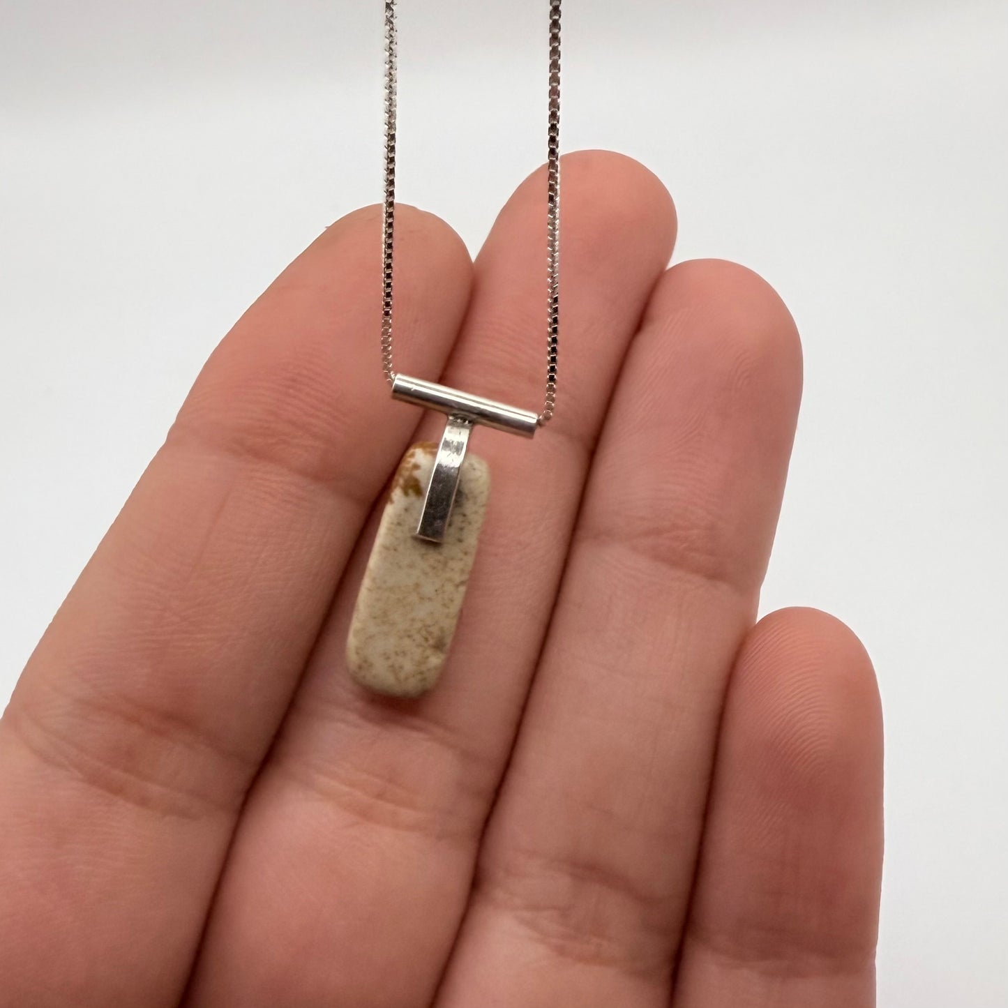 Sterling silver landscape jasper necklace shown on a hand for size, with box chain and T-bar detail