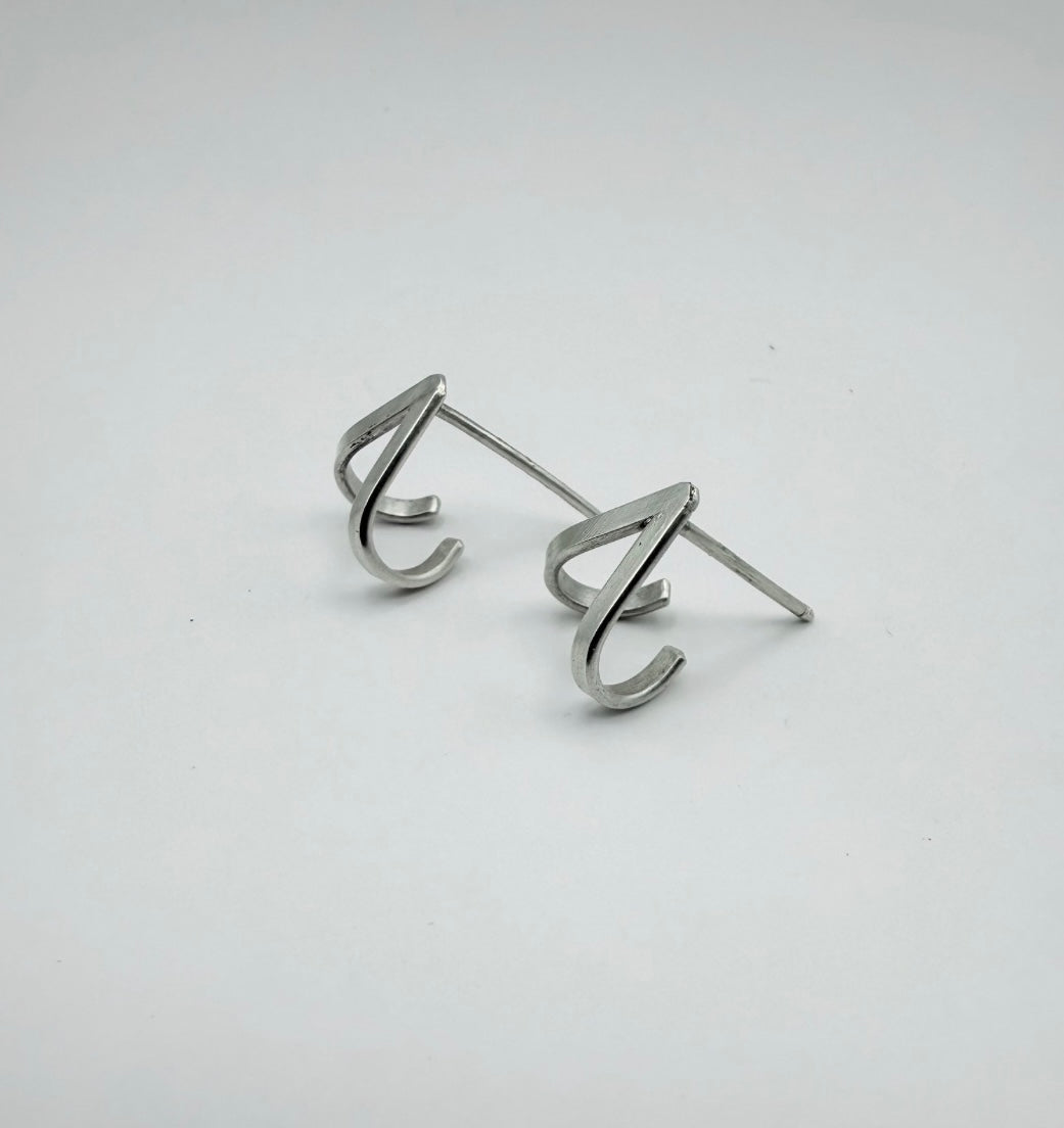 Pair of minimalist sterling silver chevron V lobe-hugger stud earrings shown from an angle, hugging the bottom of the earlobe, on a light gray background.