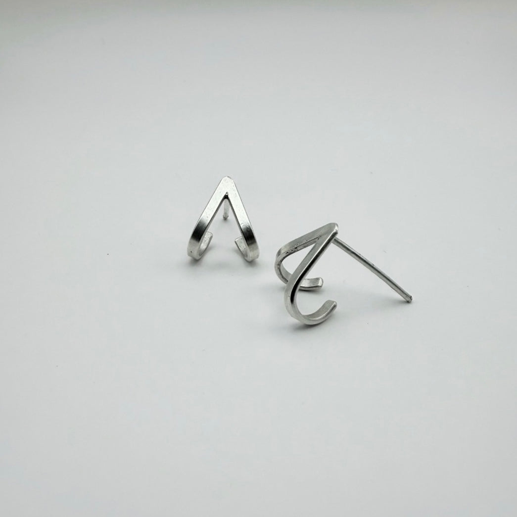 Pair of minimalist sterling silver chevron V lobe-hugger stud earrings shown from both angles, hugging the bottom of the earlobe, on a light gray background.