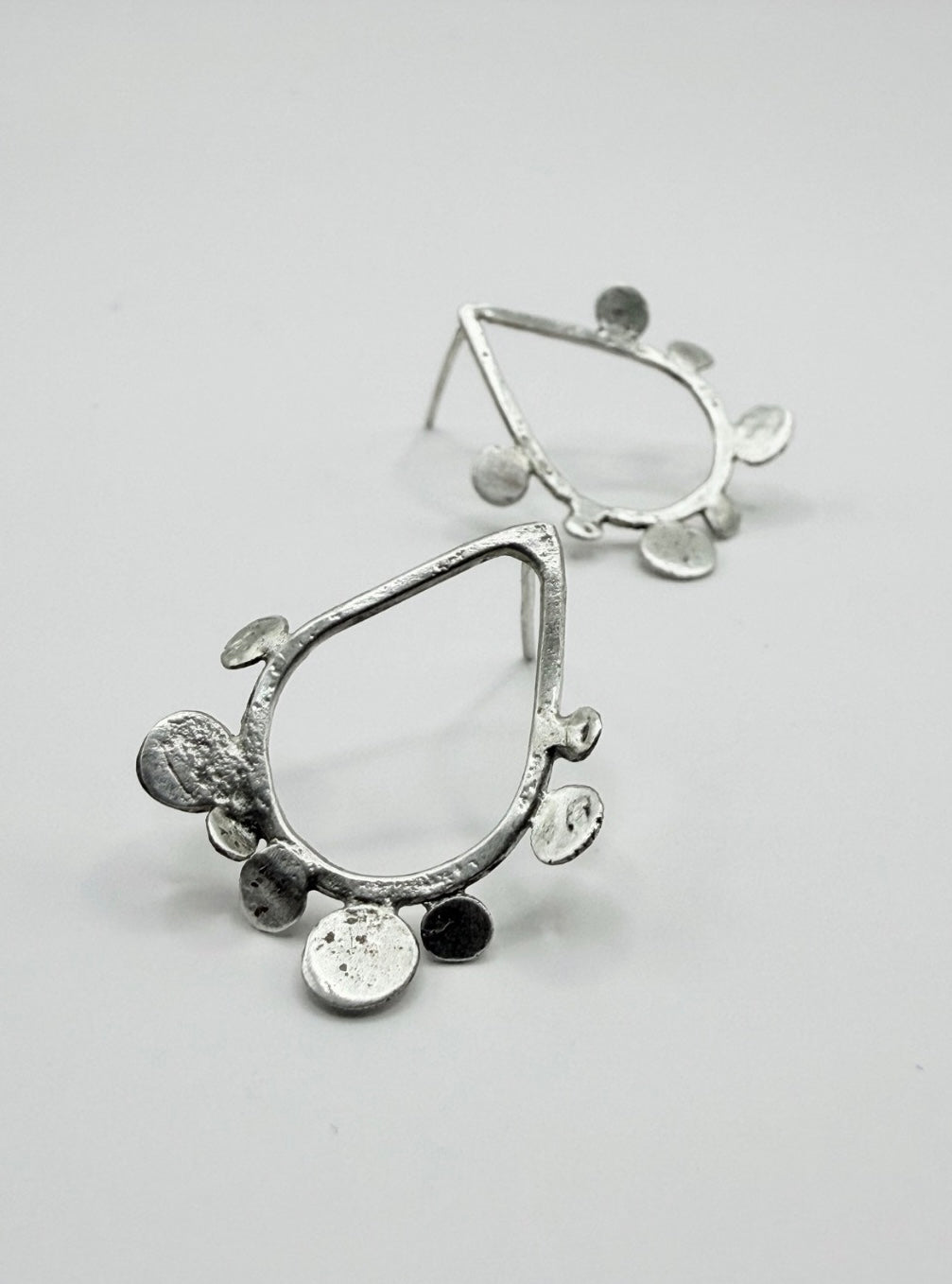 Close-up of sterling silver teardrop stud earrings with textured dot disc details on a white background