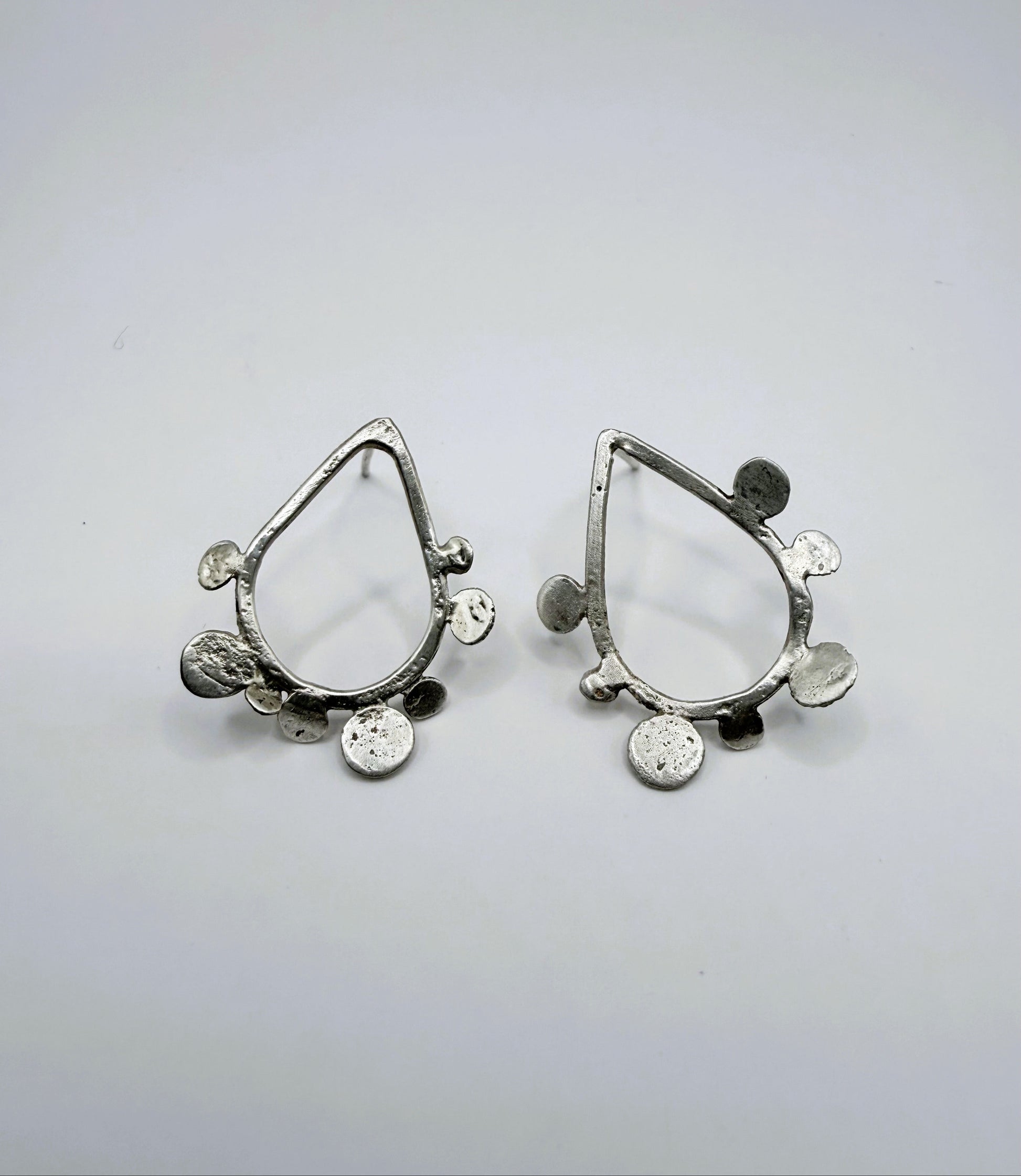 Front view of sterling silver teardrop stud earrings with textured dot disc details on a white background