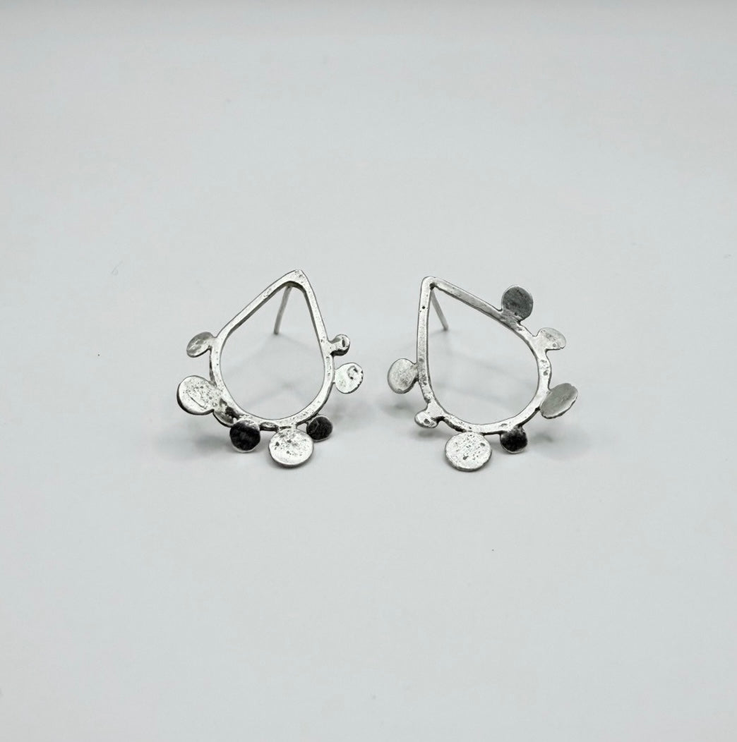 Pair of sterling silver teardrop stud earrings with textured dot disc details on a white background