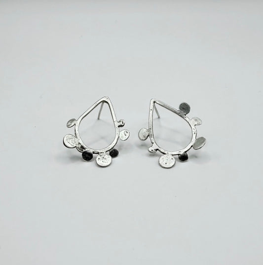 Pair of sterling silver teardrop stud earrings with textured dot disc details on a white background