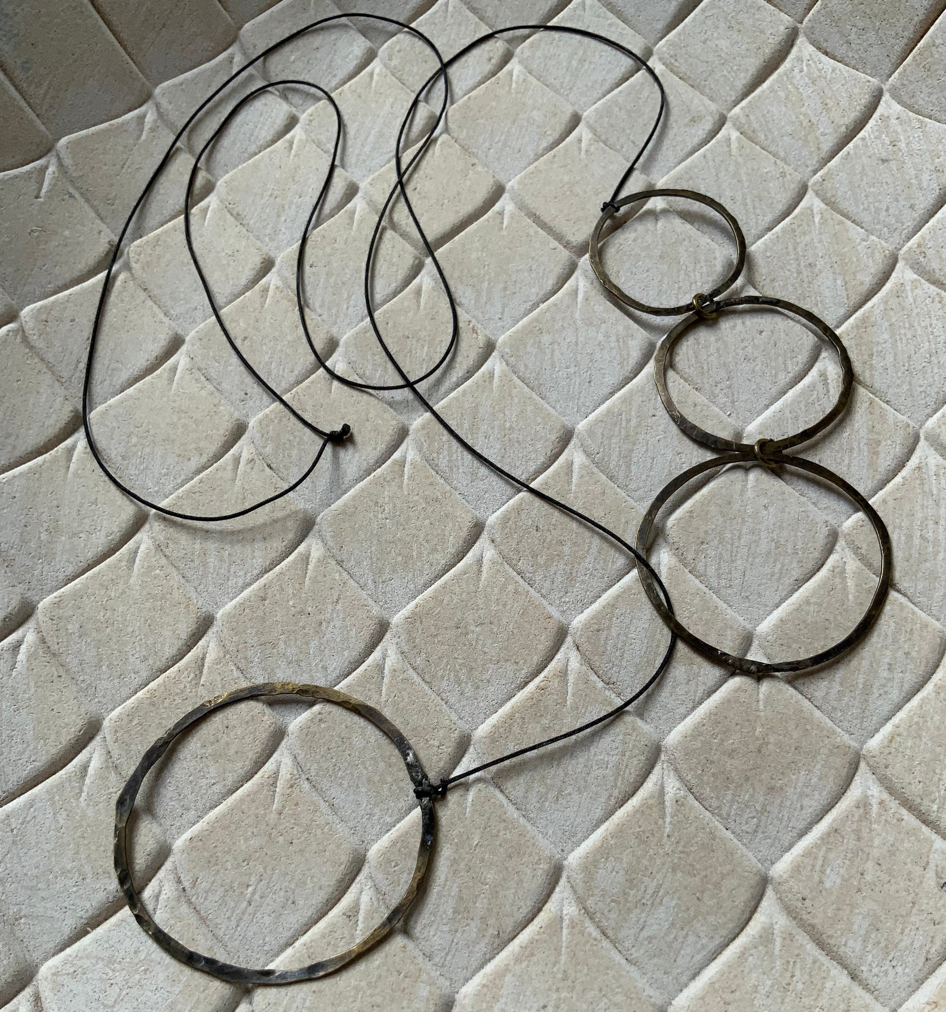 A brass necklace with cascading open circular accents, styled on a beige textured background to emphasize its modern and artistic aesthetic