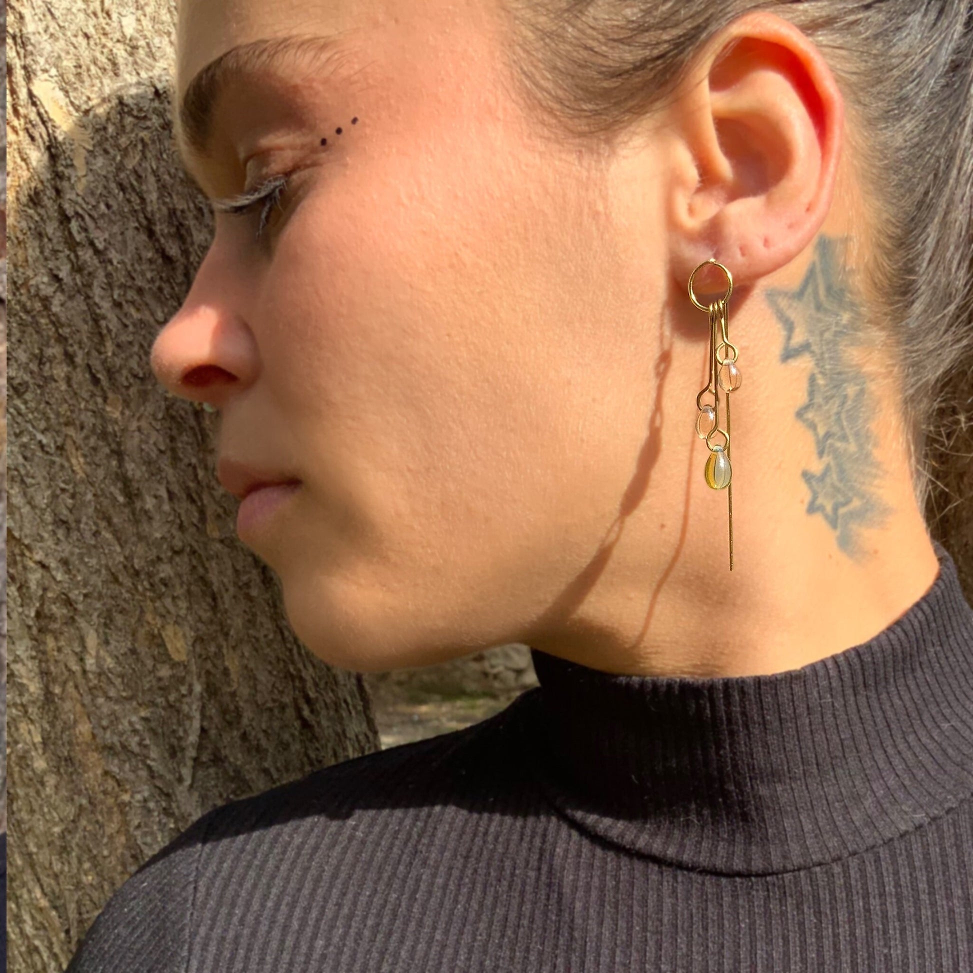 A close-up of a model wearing handcrafted gold long dangle earrings featuring clear and gradient glass pendants, styled outdoors with natural lighting for a modern and artistic look.