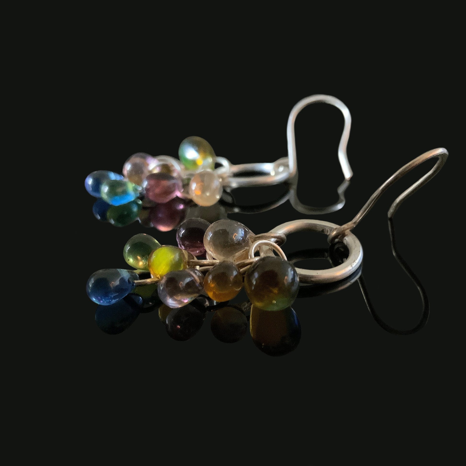 A pair of handcrafted silver hook earrings featuring multicolor glass teardrop pendants in shades of blue, green, amber, and purple, styled on a black background for a bold and elegant look.