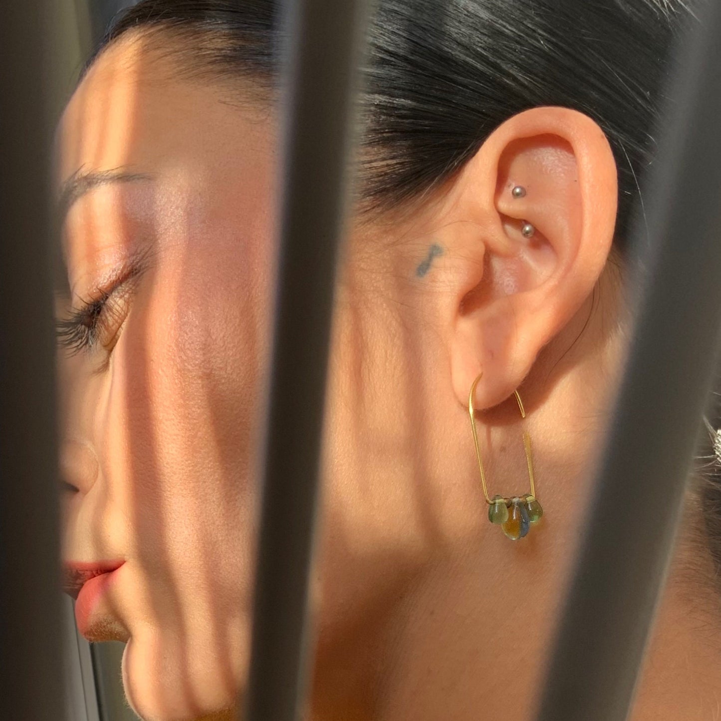 woman-profile-wearing-pair-of-silver-hoop-earrings-tulipd-shaped-with-three-multicolored-glass-teardrop-beads-hanging-from the-bottom-jewelry-by-meow-iris-collection-aurora-earrings